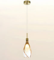 A modern single pendant light with a brushed brass ceiling canopy, cord, and cap, featuring a clear glass shade with twisted spiral edges that glow warm yellow from the light bulb inside.