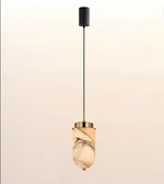 A modern pendant light with a black cylindrical ceiling canopy, a thin black cord, and a warm-toned marble-look glass shade with gold-toned metal accents, shown against a soft beige gradient background.