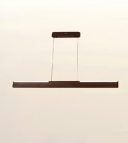 A modern linear LED pendant light with a dark brown wood-grain finish, suspended by two thin cables from a matching rectangular ceiling canopy, shown against a solid off-white background.