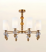 A modern six-light chandelier with a brushed gold metal frame, clear glass crystal accents, and white cylindrical fabric shades, shown against a plain light beige background.