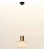 A modern pendant light with a black ceiling canopy and cord, a brushed brass cylindrical neck, and a textured white glass shade, shown against a plain off-white background.