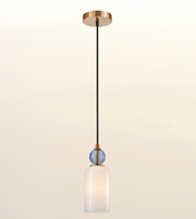 A modern pendant light fixture with a round gold ceiling canopy, a black cord, a small blue ribbed glass accent sphere, and a frosted white glass cylindrical shade, shown against a light beige gradient background.