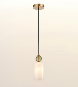 A modern single-light pendant lamp with a black cord, a round green glass bead accent, and a frosted white cylindrical shade, suspended from a brushed brass ceiling canopy against a warm off-white background.
