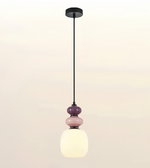 A modern pendant light fixture with a black metal rod, circular ceiling canopy, and a stacked glass shade design featuring a large frosted white globe, a smaller pink glass sphere, and a darker purple glass sphere.