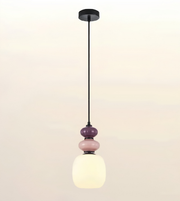 A modern pendant light fixture with a black metal rod, circular ceiling canopy, and a stacked glass shade design featuring a large frosted white globe, a smaller pink glass sphere, and a darker purple glass sphere.