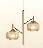 A modern two-light pendant lamp with a brushed brass/gold central pole and arms, featuring faceted clear glass shades that glow with warm light, shown against a plain off-white background.