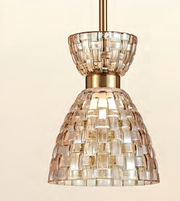 A modern pendant light fixture with a textured, woven glass shade in warm champagne tones and a brushed brass suspension rod, shown against a solid cream background.