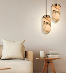 Two modern pendant lights with beige and brown marbled glass shades hanging above a sofa in a styled living room setting.