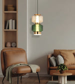 A modern two-tier pendant light hanging in a styled living room. The light features a textured clear glass top tier and a textured green glass bottom tier, both accented with brushed gold metal trim, set against a warm neutral living room background.