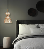 A modern pendant light with a textured, warm-toned glass shade hanging beside a bed in a dark, contemporary bedroom.