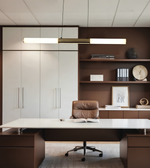 A modern office interior featuring a long white desk, a brown leather swivel chair, dark brown shelving and cabinets, and a rectangular pendant light above the desk.