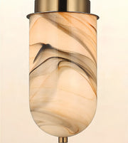 A modern pendant light fixture with a cylindrical glass shade featuring a warm beige, cream, and brown marbled swirl pattern, finished with brushed brass metal hardware at the top and bottom.
