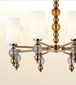 A modern multi-light chandelier with a brushed brass/gold metal frame, cylindrical frosted white glass shades, and decorative clear glass and amber-toned spherical accents, shown against a plain light background.