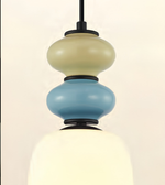 A modern pendant light fixture with a stacked, bubble-like design featuring a cream top section, a light blue middle section, and a glowing warm white bottom shade, suspended by a black rod.