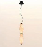 A modern pendant light with a black ceiling canopy and cord, featuring a sculptural, ribbed cylindrical shade in a warm cream or off-white tone, shown against a plain light background.