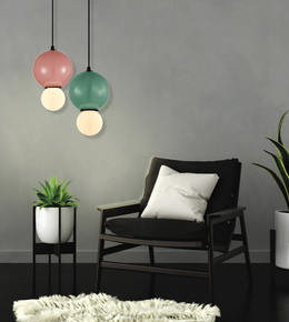 A modern living room scene featuring two hanging pendant lights with pink, green, and white globe shades, a black armchair with a white pillow, and small potted plants against a gray wall.