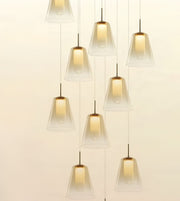 A modern multi-light pendant chandelier with nine clear glass bell-shaped shades suspended at varying heights against a warm off-white background.