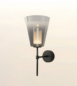 A modern wall-mounted sconce with a translucent smoky gray glass shade, a black metal stem, and a round black wall plate, shown lit against a soft off-white background.