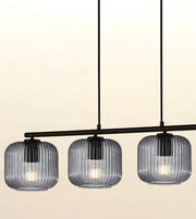 Three-light linear pendant chandelier with ribbed clear glass shades and a black metal frame, shown against a warm off-white background.