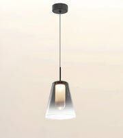 A modern pendant light with a tapered clear glass shade and a black ceiling canopy and cord, shown against a plain light beige background.