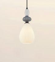A modern pendant light with a textured white teardrop-shaped shade, a ribbed gray middle section, a frosted white bulb, and a black hanging cord against a warm off-white background.