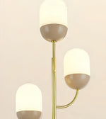 A modern three-light floor lamp with a slim gold metal frame and frosted white dome-shaped glass shades, each paired with a taupe-colored base, shown against a plain light beige background.