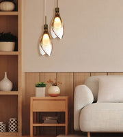 Two modern pendant lights with white leaf-shaped glass shades and bronze metal accents, hanging in a warm, contemporary living room next to a light-colored sofa and wooden side table.
