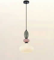 A modern pendant light fixture with a black ceiling canopy and cord, featuring a sculptural design with a muted sage green bulb, a pink ribbed accent, and a ribbed white glass shade.