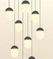 Modern multi-light pendant chandelier with matte black acorn-shaped caps and frosted white cylindrical shades hanging at varying lengths against a warm off-white background.