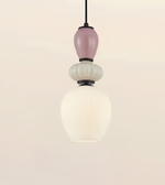 A modern pendant light fixture with a black cord, a dusty pink glass bulb, a textured white glass bulb, and a large ribbed white glass shade below, set against a solid light beige background.