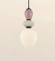 A modern pendant light fixture with a black cord, a dusty pink glass bulb, a textured white glass bulb, and a large ribbed white glass shade below, set against a solid light beige background.