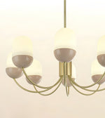 A modern six-light chandelier with curved brass-toned metal arms and frosted glass shades that are warm cream on top and taupe below, shown against a plain off-white background.