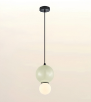 A modern pendant light fixture with a matte black ceiling canopy and cord, featuring two stacked frosted glass globes, one pale green and one glowing warm white, shown against a soft beige gradient background.