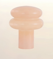 A translucent peach-colored silicone or rubber cap with a rounded, tiered design and a cylindrical base, shown against a solid off-white background.