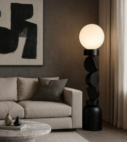 Black sculptural floor lamp with opal globe beside modern sofa in living room