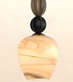 A modern pendant light with a marbled glass shade in warm cream and tan tones, accented by a matte black spherical ornament and a dark brown metallic cap at the top, set against a solid off-white background.