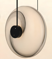 A modern circular pendant light with a frosted glass disc and a black central suspension hardware, shown against a plain light beige background.
