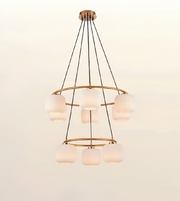 A modern multi-tier chandelier with five frosted glass shades and a brushed brass/gold metal frame, suspended by black cords against a plain off-white background.