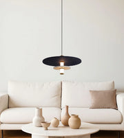 Modern black pendant light above cream sofa and round table with ceramic vases in minimalist living room