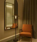 Orange chair in a room with a tall floor lamp and a large mirror on the wall.